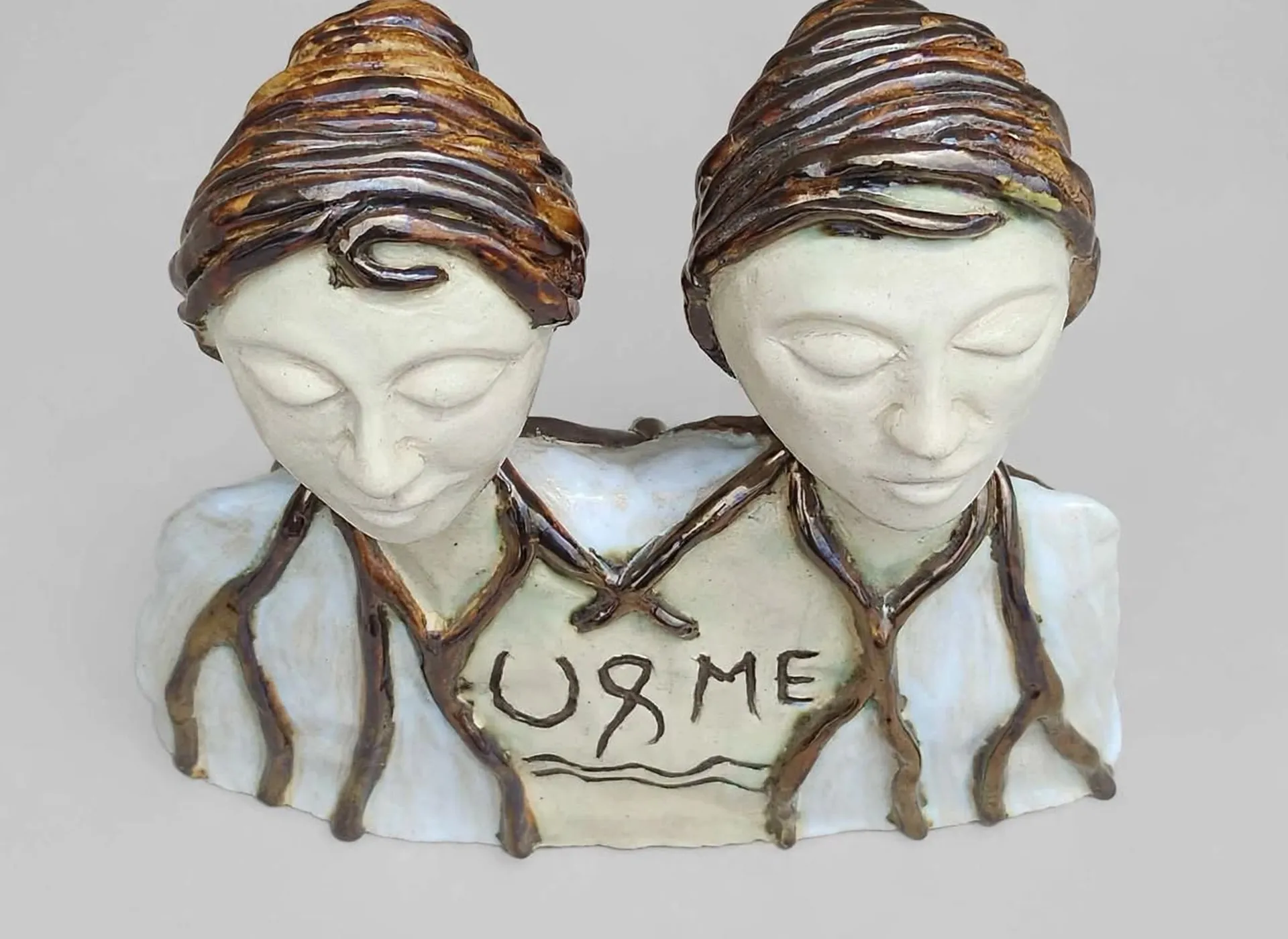 'U & Me' — a hand-built ceramic sculpture of two figures, closed-eyed, with the words U and ME incised across their chests
