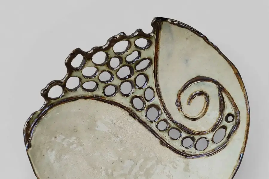 Detail of a perforated cream ceramic dish with a spiral cutout pattern