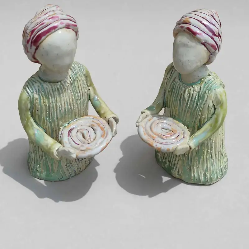 Two ceramic attendant figures in striped turbans, each holding a spiral-painted plate