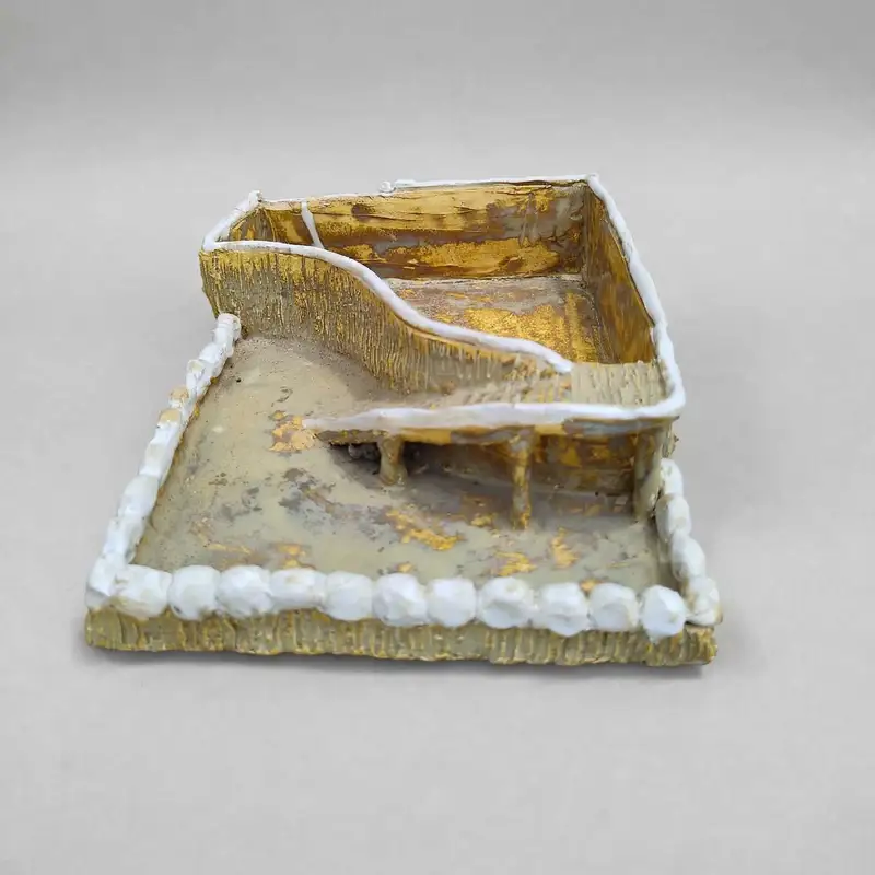 Small gilded ceramic courtyard diorama with a pillared walkway and white pebble border