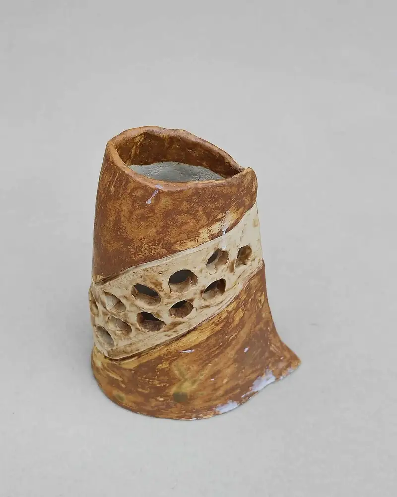 Tall rust-brown ceramic vessel with a diagonal perforated cream lattice band